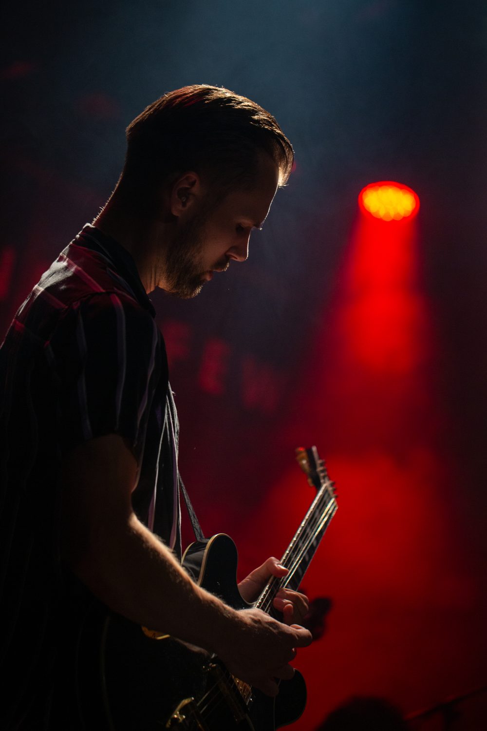 Gitarist in silhouet tegen een rode lichtbundel op het podium
